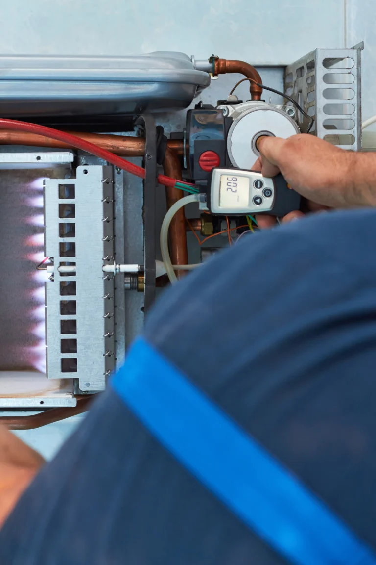 Technician performing boiler maintenance by adjusting the thermostat on a gas boiler, with visible flames flickering inside the unit.