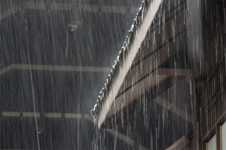 Rain pours off a slanted roof edge, creating streaks against a dark background, while the sump pump works tirelessly below to keep the basement dry.